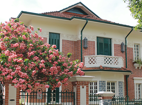 Imagem de uma casa, com tijolos à mostra, atrás de um ipê rosa.